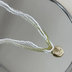 Détail du collier double rang perles blanches et vertes avec pendentif médaille rose