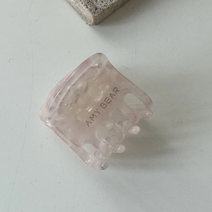 Détail d'une pince à cheveux rose translucide avec le logo Amy Bear et une finition mate