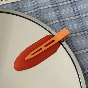 Close-up of dual-tone matte red and orange seamless duckbill hair clip on a mirror