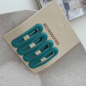 Detail showing set of four matte teal BB hair clips on display card with soft texture