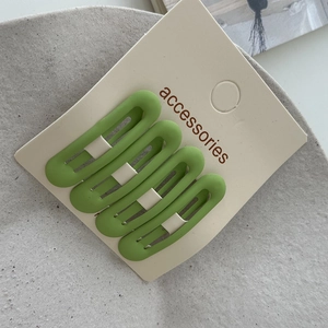 Detail of four matte grass green rectangle hair clips displayed on a white product card