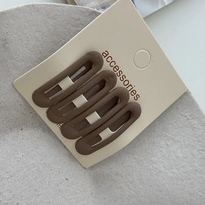 Close-up of four matte coffee-colored oval hair clips on an accessories display card