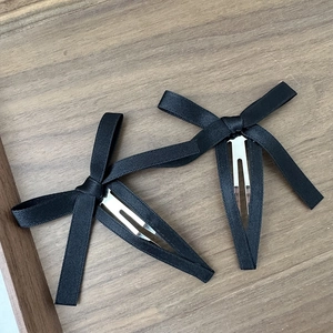 Dettaglio di due fermagli per capelli a fiocco in raso nero con clip BB argentate