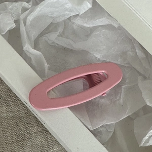 Dettaglio di un fermaglio per capelli ovale rosa opaco su confezione di carta bianca