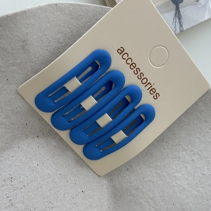 Detailed view of four matte navy blue snap hair clips set on cream cardboard packaging