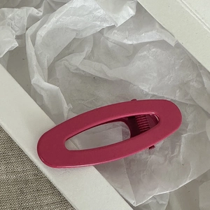 Dettaglio di un fermaglio per capelli ovale traforato magenta opaco su sfondo bianco