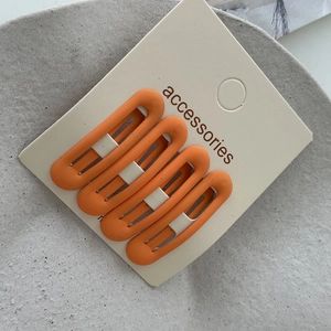 Close-up of four matte orange oval snap hair clips on a white accessories display card