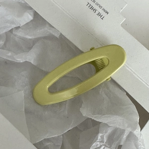 Dettaglio macro della clip per capelli ovale traforata verde chiaro opaco su carta