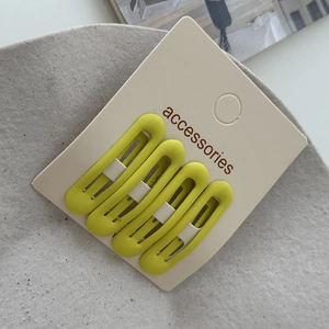 Close-up of four matte neon yellow oval hair clips on a white display accessories card
