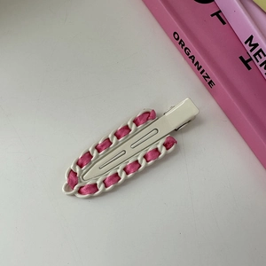 Detalle de pinza de pelo de metal blanco con cinta de raso rosa tejida en la cadena