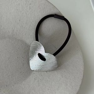 Détail macro d'un charm cœur en argent avec texture brossée sur élastique à cheveux