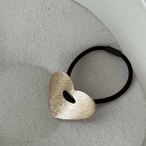Détail d'un charme coeur en métal doré brossé sur un élastique à cheveux noir robuste