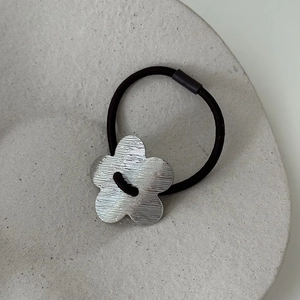 Détail d'une fleur en métal brossé sur un élastique noir dans une coupelle en céramique