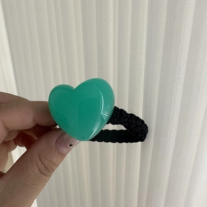 Detail shot of heart-shaped resin charm and black braided elastic hair tie in green