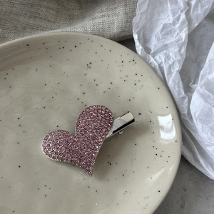 Λεπτομέρεια από κλιπ μαλλιών καρδιά με ροζ στρας σε μπεζ διακοσμητικό πιάτο
