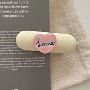 Détail d'une pince à cheveux crème avec un cœur rose et l'inscription Lover sur tissu