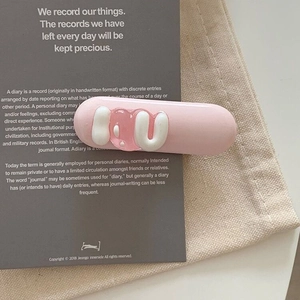 Gros plan d'une pince à cheveux rose en forme de capsule avec des lettres 3D en gelée
