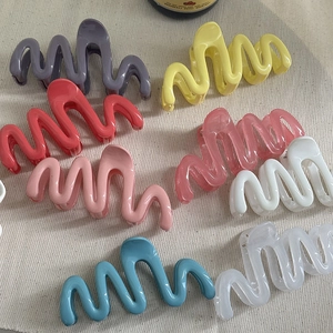 Colorful wave-shaped hair claws in vibrant resin colors on a textured cream background