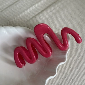 Detailed close-up of vibrant pink wavy hair claw clip on a white shell plate decoration