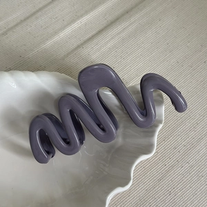 Detail of purple-grey wave hair claw clip on a white shell-shaped decorative ceramic plate