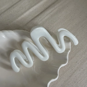 Close-up of a white wavy hair claw clip displayed on a shell-shaped ceramic tray