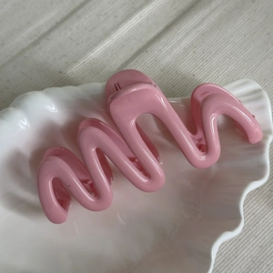 Detailed view of glossy pink wavy hair claw clip resting on a white ceramic shell tray