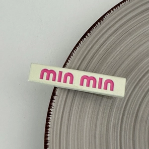 Close-up of matte beige resin hair clip with pink lettering on ceramic tray