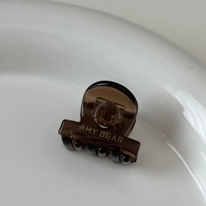 Vue macro détaillée d'une mini pince à cheveux en acétate ambre avec le logo AMY BEAR doré