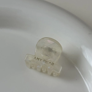 Gros plan d'une mini pince à cheveux en acétate crème avec le logo AMY BEAR sur plat