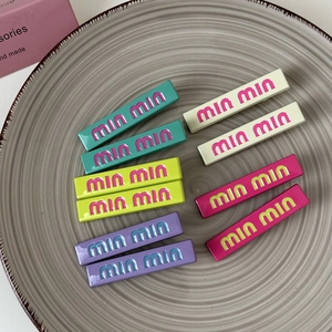 Detailed macro view of colorful metal hair clips with embossed letters in five vibrant colors