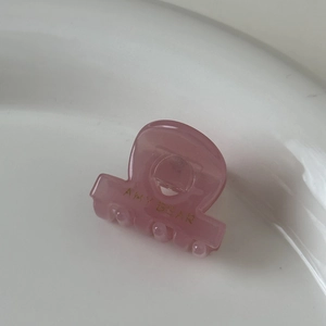 Détail macro d'une petite pince à cheveux rose en acétate avec texte doré AMY BEAR