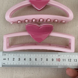 Detail view of two pink acrylic heart hair claws on textured fabric with a measuring ruler