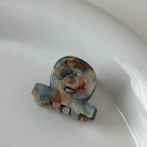 Détail d'une mini pince à cheveux en acétate AMI BEAR avec texture marbrée et lettrage doré