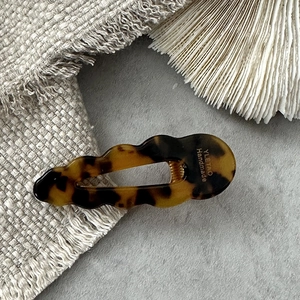 Detail of wave-edged acetate hair clip with tortoise shell pattern and gold metal clip
