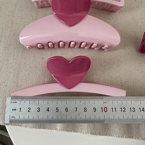 Detailed view of pink heart hair claws in two sizes with glossy finish on beige fabric