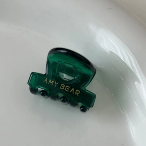 Détail d'une mini pince à cheveux en acétate vert foncé avec logo doré et dents noires
