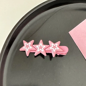 Détail d'une pince à cheveux étoile Y2K rose et blanche sur un plateau noir