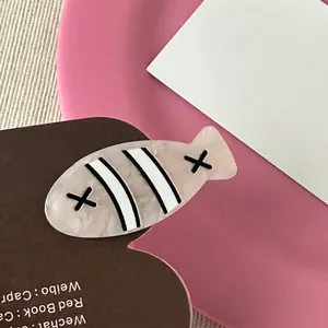 Detailed close-up of fish-shaped hair clip with cream marble texture and black accents