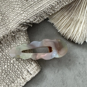 Close-up of wavy acetate hair clip with marble textures and golden metal duckbill base