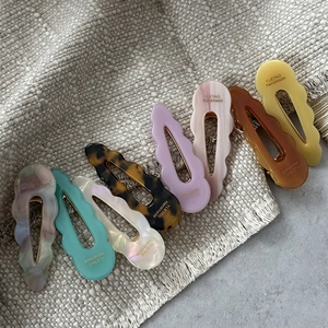 Minimalist wavy acetate hair clips in eight assorted colors on a textured background