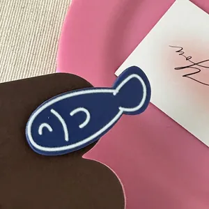 Close-up of a navy blue fish hair clip with a matte finish on a pink display