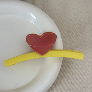 Detail of a yellow hair claw clip with red heart design on a white ceramic plate
