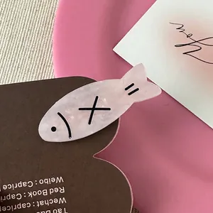 Detail of pink fish-shaped hair clip made of acetate with black lines and X pattern