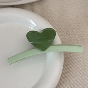 Detail of light green heart hair claw clip resting on a white ceramic plate tray