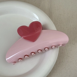 Top view of a pink resin shark clip with a dark pink heart on a white ceramic plate