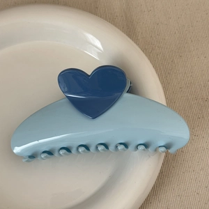 Close-up of blue heart hair claw clip on white ceramic plate with beige fabric