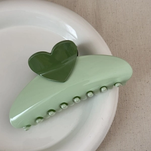 Close-up of green heart claw clip with premium polished finish on a white plate