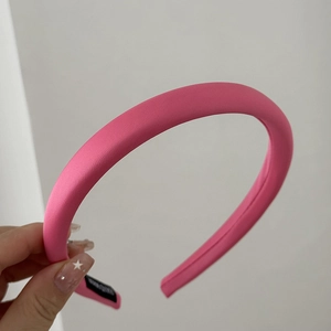 Detail of a bright pink handmade padded headband with glossy satin finish and woven label