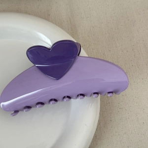 Detail view of a dual-tone purple heart hair claw clip on a white ceramic plate