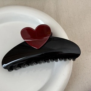 Close-up of a black heart-shaped hair claw clip on a white ceramic plate and linen cloth